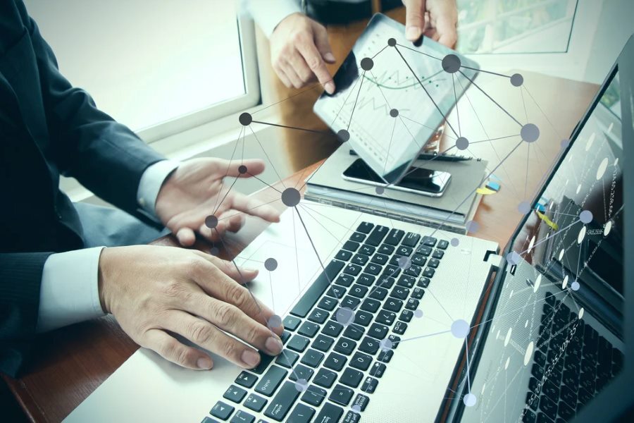 business documents on office table with smart phone and digital tablet and stylus and two colleagues discussing data in the background_RD
